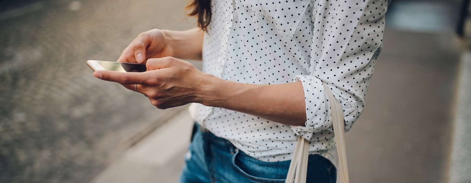 woman walks down the street and texts with a bag of groceries on her arm